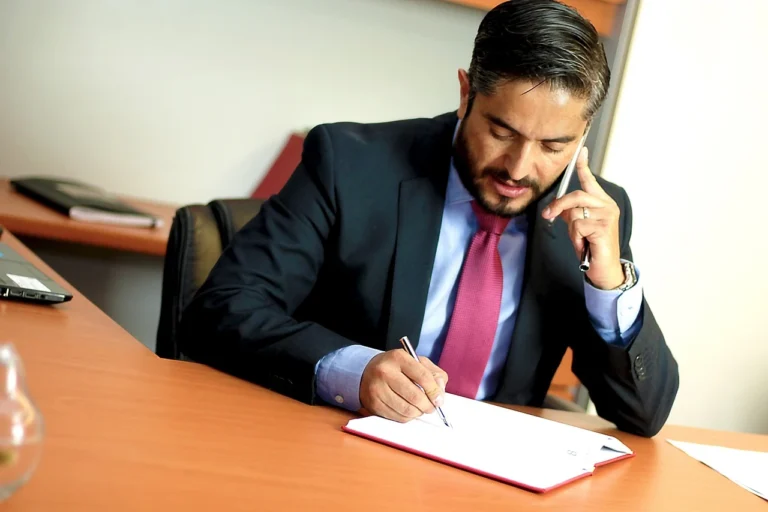 Homem de negócios estudando documentos importantes enquanto fala ao telefone em escritório moderno.